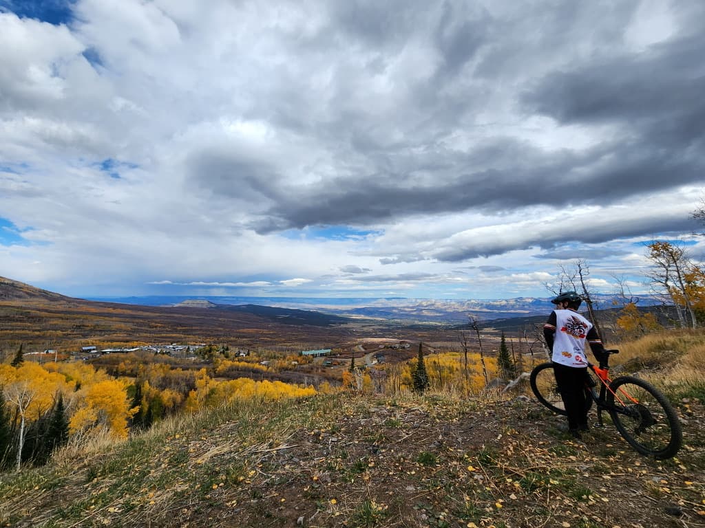 Matthew with his mountain bike in a Jax State Cycling Club jersey, looking across the autumn mountains in Colorado
