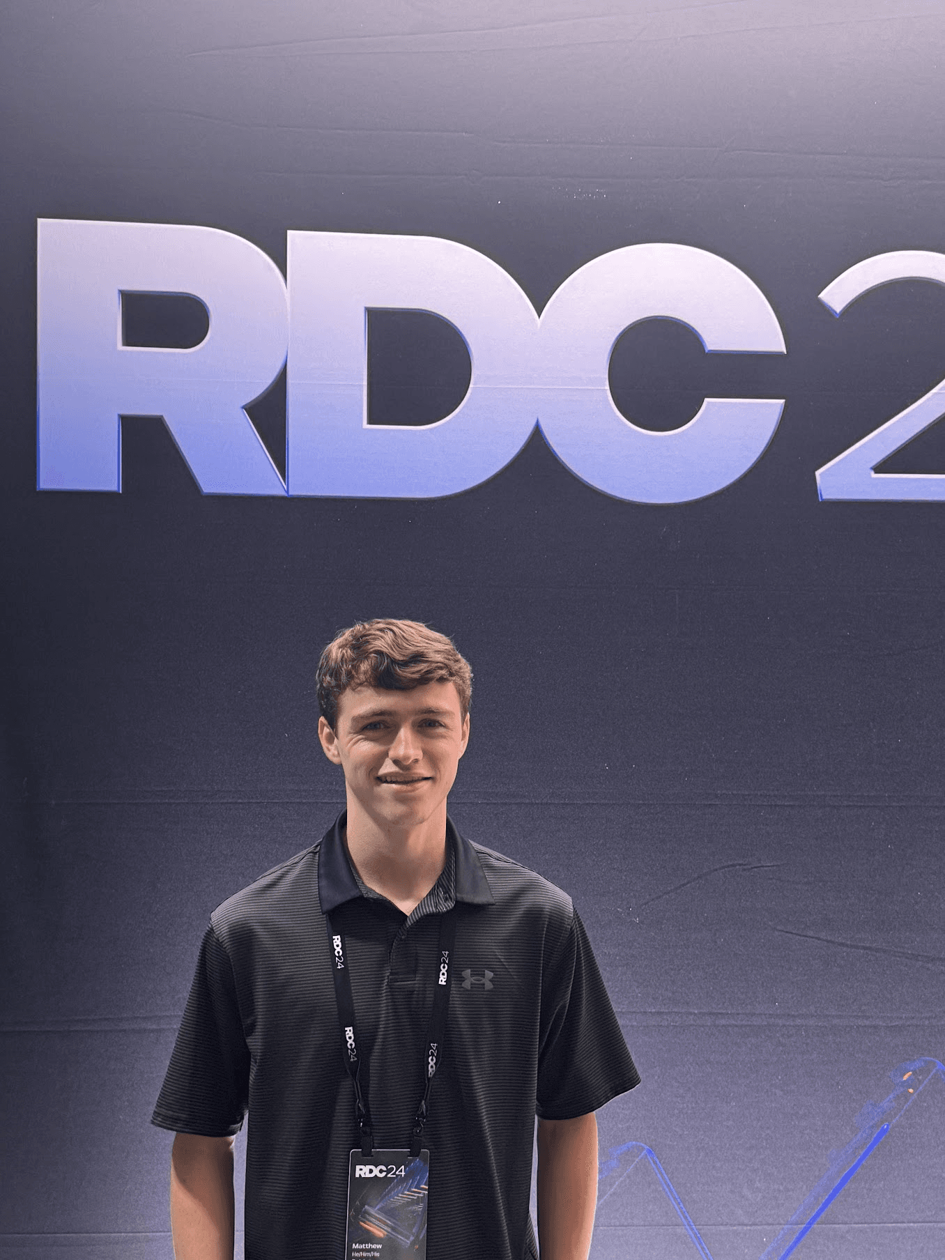 Matthew wearing his RDC24 badge in front of the conference backdrop