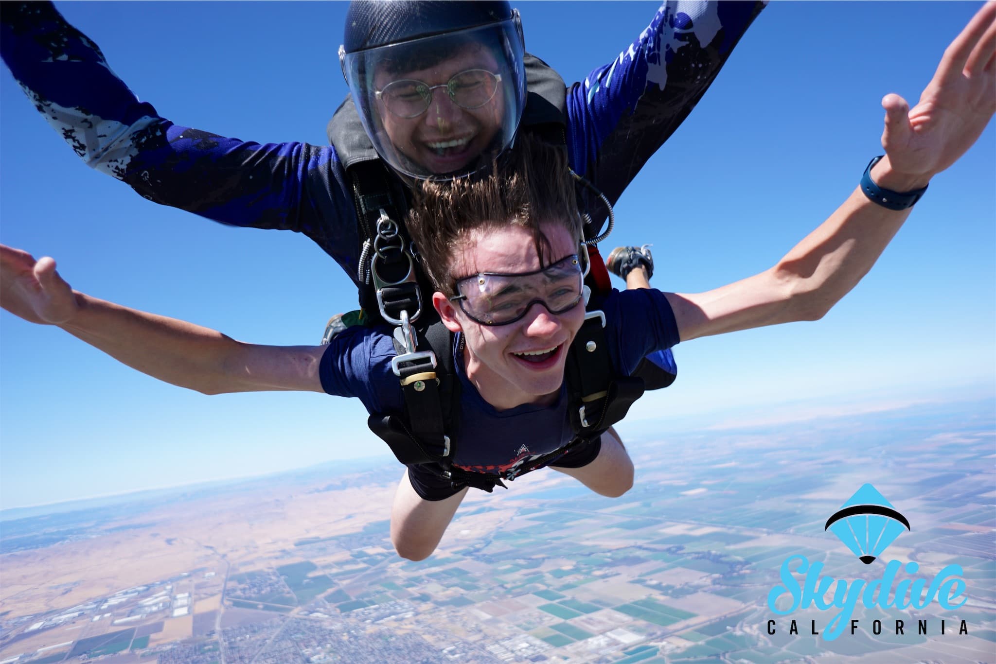 Matthew smiling with his arms out during a tandem skydive above the California landscape