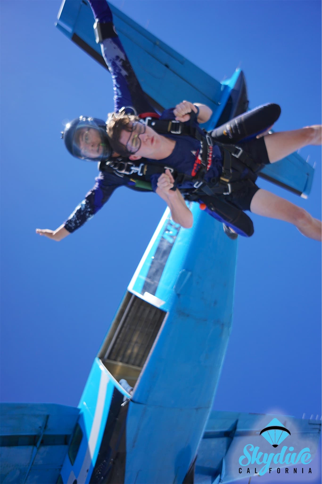 Matthew just after leaving the plane on a tandem skydive, with the blue plane still directly behind him